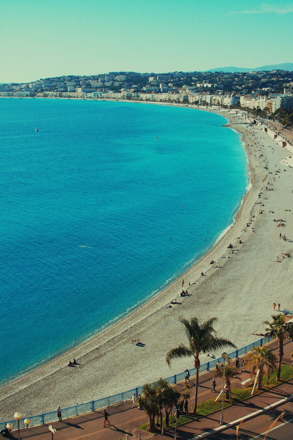 Turquoise Mediterranean water curves along the Nice waterfront and palm-lined promenade