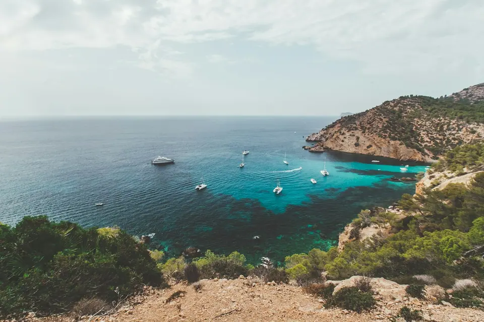 Sailboats anchored in a turquoise Mallorca cove framed by rocky Mediterranean cliffs